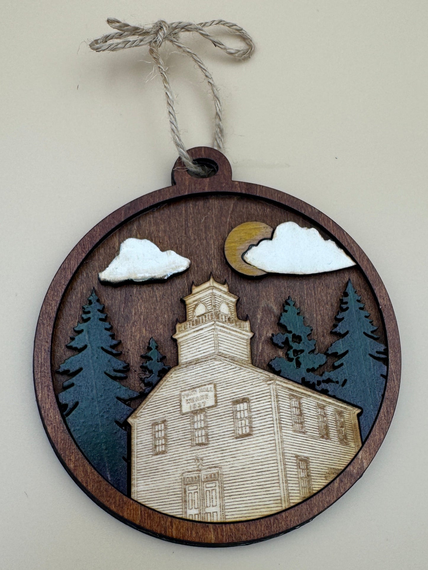 A 3.75 x 4.2 inch round wooden ornament featuring a laser-cut layered landscape with the Town Hall of Weare, New Hampshire, trees, clouds, and a moon, hanging from a twine string against a plain beige background.